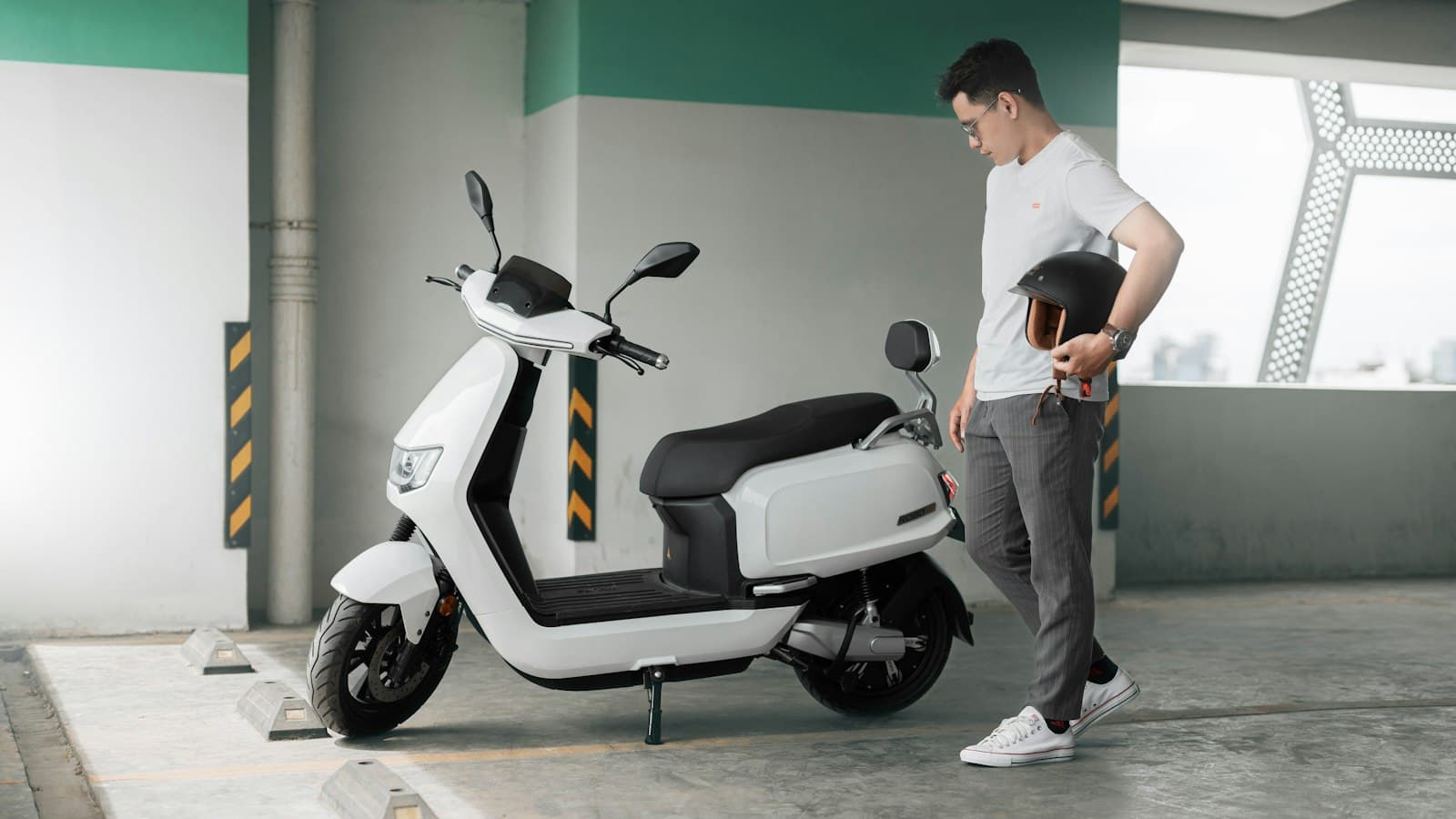 Scooter elétrica branca estacionada, com o dono segurando o capacete ao lado